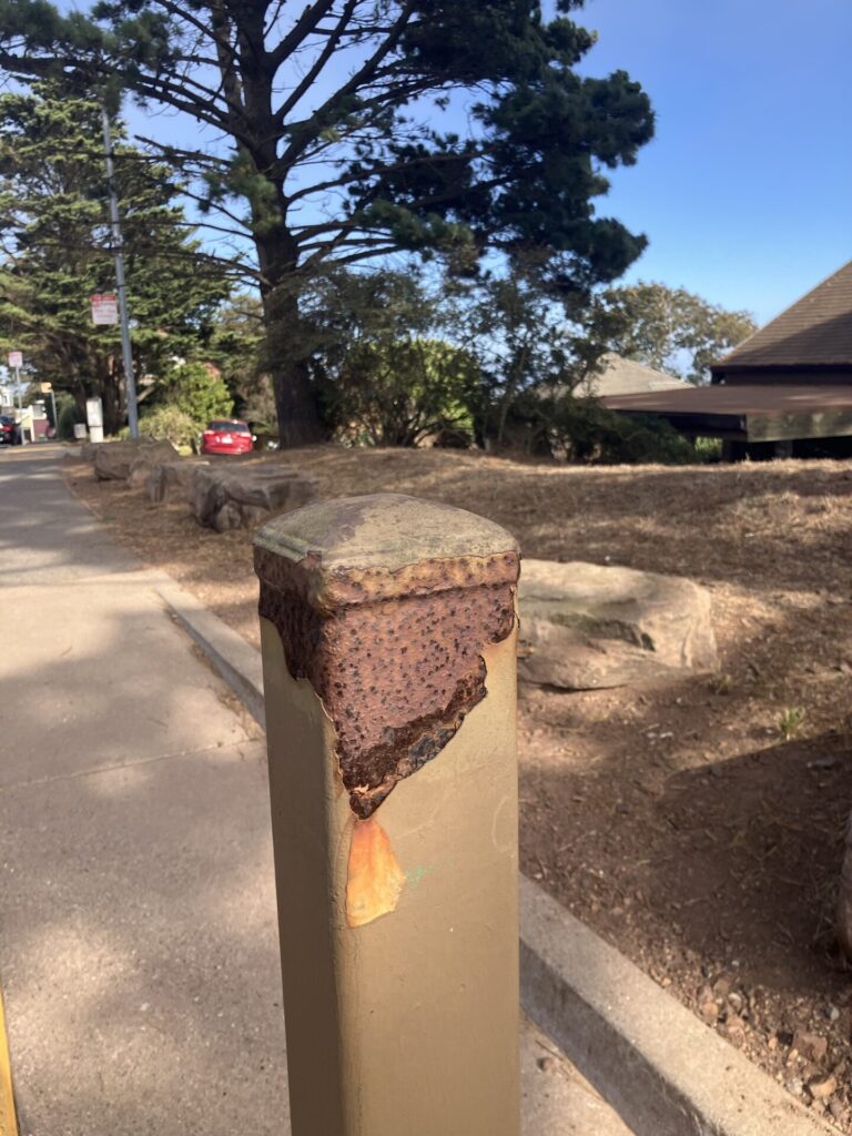 Bollard with paint chipped away and rust that looks like an erupting volcano. 